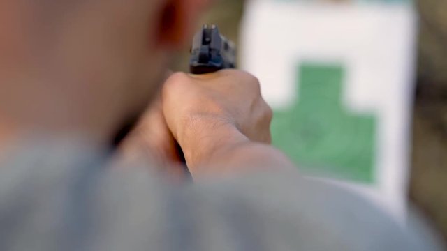 Young man is shooting from a gun at the target, close up