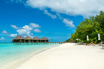 Beautiful tropical landscape. Wooden villas over water of the Indian Ocean. Sandy beach with sunbeds and umbrellas.