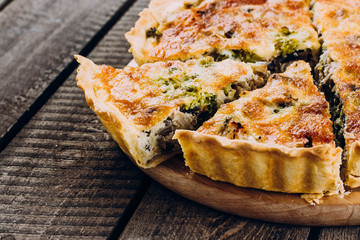 Quiche Lorraine with chicken and vegetables on rustic dark table background. Pie with mushrooms, chicken and broccoli on wooden kitchen board. Traditional French food. Close up, copy space