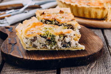 Quiche Lorraine with chicken and vegetables on rustic dark table background. Pie with mushrooms, chicken and broccoli on wooden kitchen board. Traditional French food.