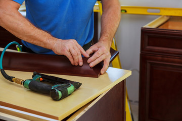 Carpenter brad using nail gun to Crown Moulding on kitchen cabinets framing trim