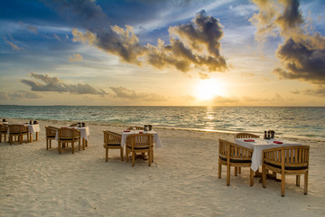 Tropical restaurant on the sandy beach. Landscape of beautiful sunset in Maldives island with colorful sky and dramatic clouds over wavy sea.