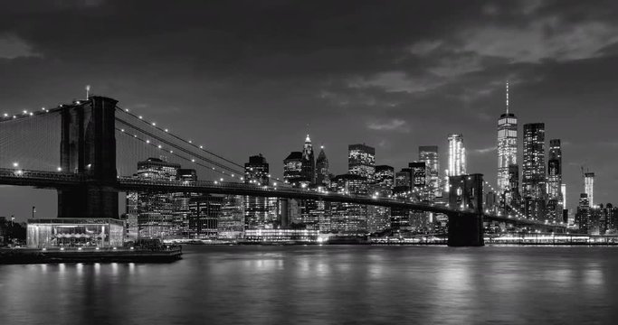 Time-lapse of Lower Manhattan Financial District skyscrapers, Brooklyn Bridge, and East River with passing clouds at twilight in Black & White. Manhattan, New York City