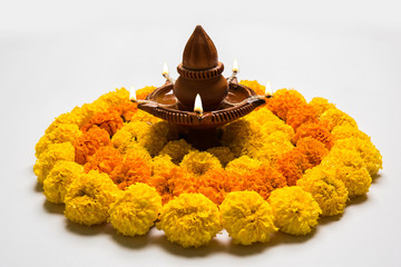 flower rangoli for Diwali or pongal or onam made using marigold or zendu flowers and red rose petals over white background with diwali diya in the middle, selective focus
