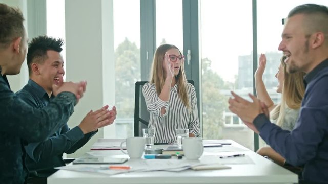 Diverse group of creative business team members with female team leader celebrating with high fives at a startup in a modern office in slow motion