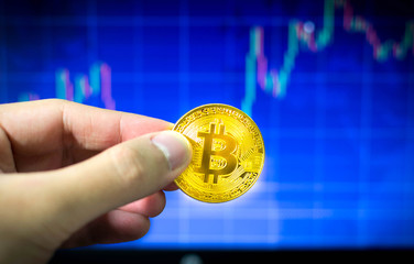 Man holding gold bitcoin and BTC trading chart in background, Financial concept