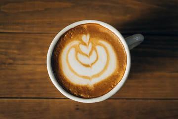 Fresh coffee latte art in white cup on wooden table.