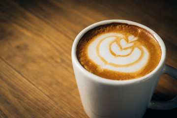 Fresh coffee latte art in white cup on wooden table.