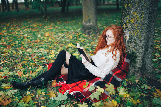 Redhead Girl Reading The Book In Autumn Park