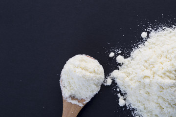 Powdered milk and wooden spoon on the black background. Top view.