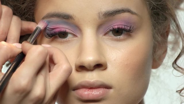 Visagist applying eyeshadow close up. Girl having makeup done.