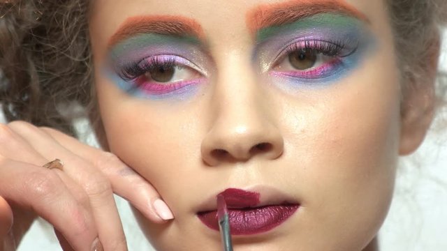 Visagist is using lipstick brush. Female model, colorful artistic makeup.