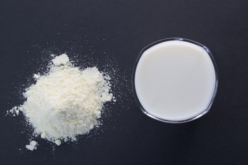 Powdered milk and glass cup of milk on the black background. Top view.