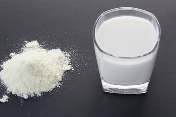 Powdered milk and glass cup of milk on the black background.