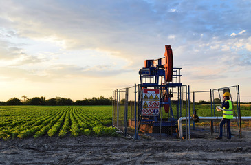 A female engineer at work on an European oil well during dusk time, agriculture field in background    