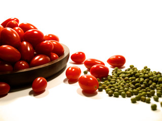 Isolated pile of cherry tomato in a dark wood plate and mung beans in white background