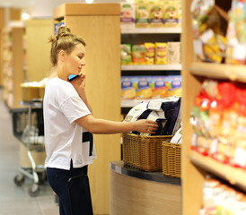 Woman shopping in supermarket reading product information. Checking list.Woman with a smartphone  choosing  a dairy products at supermarket 
