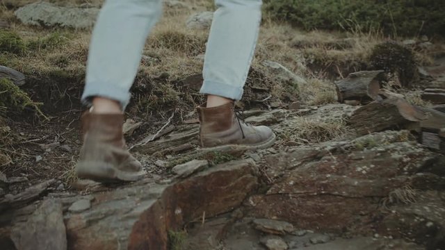 Close up following shot of female in denim jeans and leather heavy duty boots, walking or hiking or exploring rocky difficult trail on mountain terrain, concept tourist, nomad, adventure