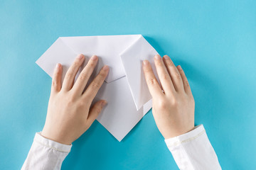 Person's hands folding a paper airplane on a blue background