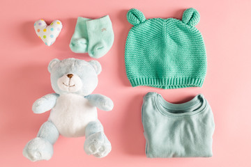 Baby clothes and teddy bear on a pink background
