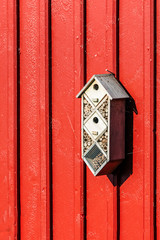 Small insect hotel or bug hotel on red wooden wall.
