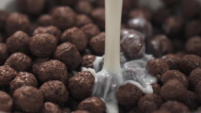 Slow motion milk pour into bowl with chocolate cereal balls
