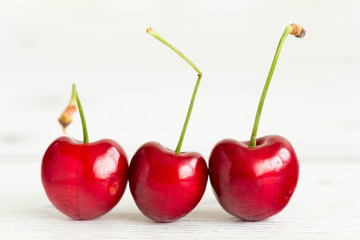 Three fresh, juicy cherries in line, white background