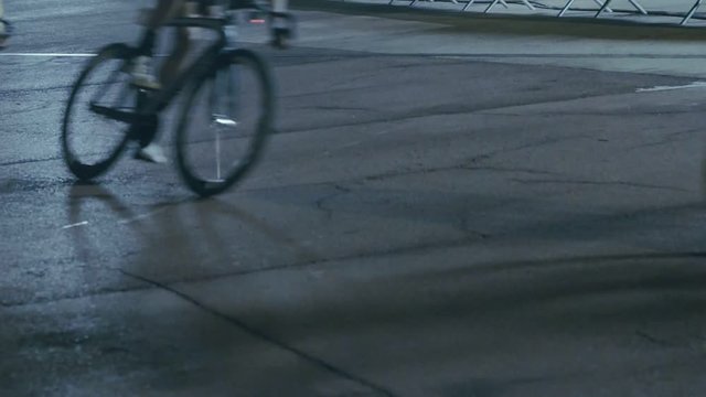 Slow motion night video of road cyclists riding criterium on fast paced course, swooshing in front of camera, leaning inside curves and overlapping competitors, fast and fearless