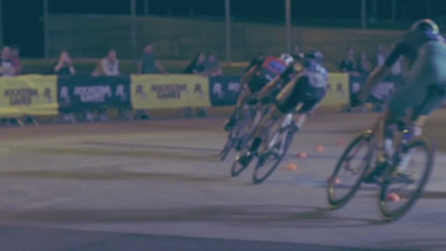 Slow motion shot of professional racers riding their carbon road bikes during nocturnal criterium with photographers camera flashes on them