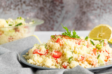Healthy couscous salad with herbs and vegetables on grey background