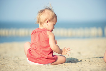 Baby playing on the sandy beach near the sea. Cute little girl in red dress with sand on tropical beach. Ocean coast.