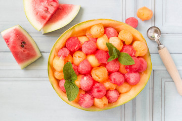 Ripe, juicy, colorful melon balls, served in a watermelon peel with mint leaves, top view