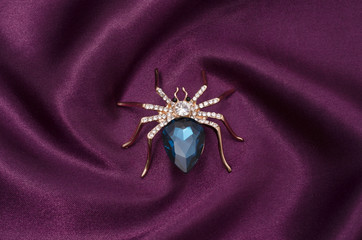 Golden spider with a big blue stone on silk fabric