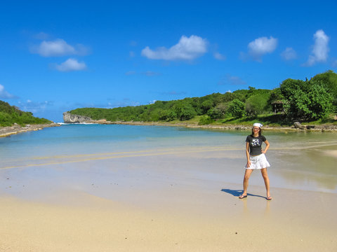 Young and smiling woman with white skirt and bandana, posing on shoreline of the popular tourist attraction of Porte d'Enfer Beach, Guadeloupe, French West Indies. 