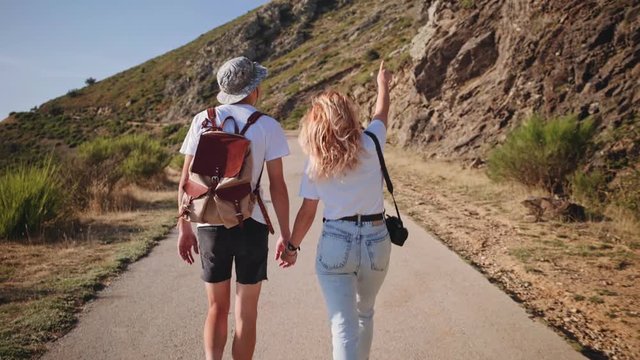 Pretty beautiful people, in trendy outfits, hipster backpack and camera, they hold hands and look around natural surroundings, urban nomads living inspiring adventures