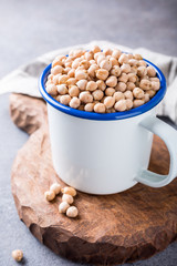 Raw uncooked organic chickpeas in white enamel mug on rustic wooden board on light gray stone background. Healthy vegan vegetarian food concept