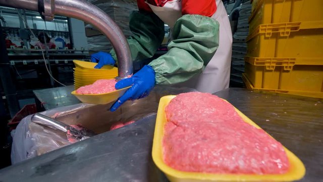 A worker uses many plastic trays to pack ground meat. 