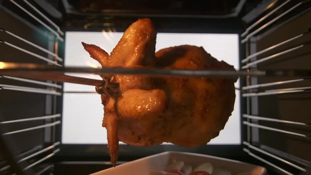 Cooking roasted whole chicken on the rotisserie spit in hot convection oven timelapse. Crispy golden chicken turning under a grill element. View from inside of the electric cooker.