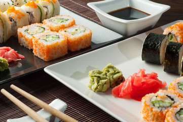 Sushi on a black and white plate, on a wooden mat with chopsticks and soy sauce