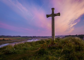 Fototapeta na wymiar The Wooden Cross on Church Hill, Alnmouth, Northumberland, England. UK. The hill is the site of the long ruined church of St Waleric. At sunrise/ dawn with a colourful dawn sky.