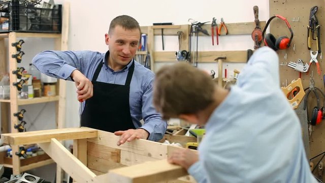 teacher and boy chiselling a wooden bench in workshop
