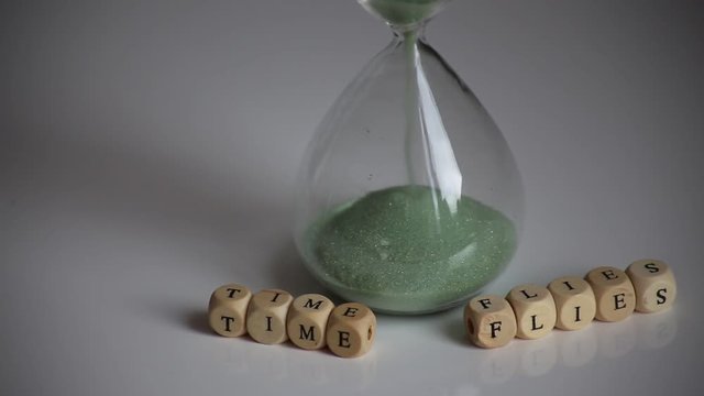 "Time Flies" mit Holzbuchstaben vor ablaufender Sanduhr