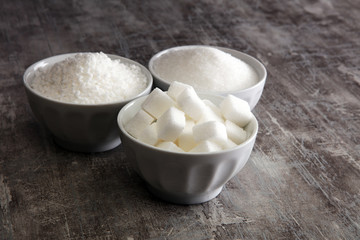 Bowl with white sand and lump sugar on grey background