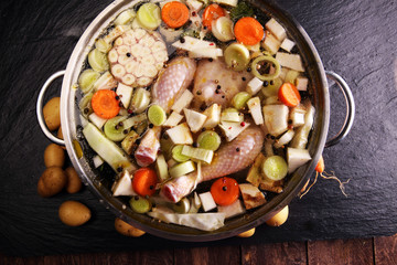 Bone broth made from chicken with carrots, onions various fresh vegetables in a pot - colorful fresh clear spring soup. Rural kitchen scenery bouillon or stock