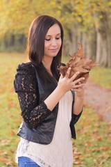 Schöne junge Frau sammelt verträumt bunte Herbst Blätter im Wald. Herbstlicher Herbsttag mit buntem Laub. Das Mädchen träumt verliebt von der Liebe zur Natur und geniesst Jugend, Glück und Freude