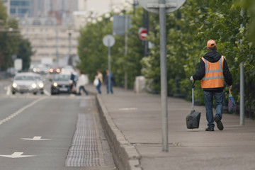 Road sweeper worker walking along city street with broom tool in Russian megapolice