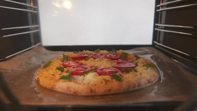 Cooking baked italian pizza in hot convection oven timelapse. Closeup of frozen pizza topped with tomatoes mozzarella and edam cheese baking inside hot oven. View from inside of the cooker