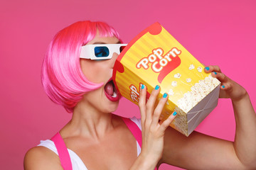 femme avec perruque rose et lunettes 3D au cinéma mangeant du pop-corn