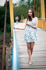 Girl with long hair and curls in a dress standing on suspension bridge