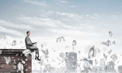 Man on roof edge reading book and symbols flying around